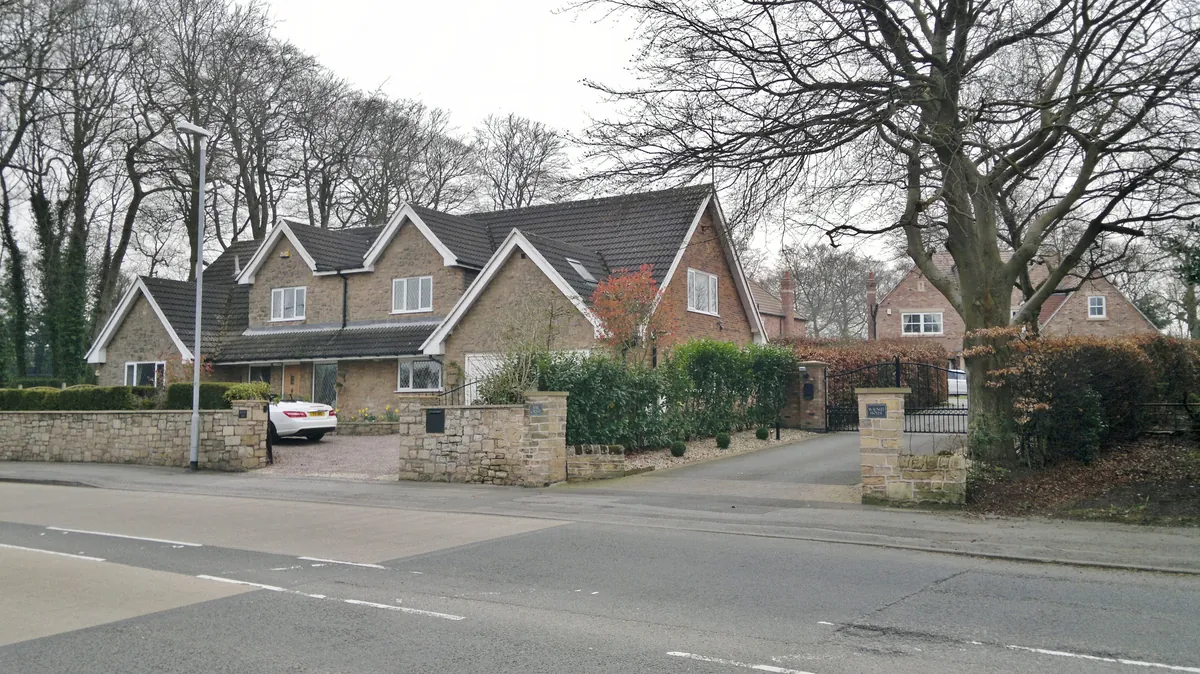 A large detached house behind stone walls and hedges on High Oakham Hill in Mansfield