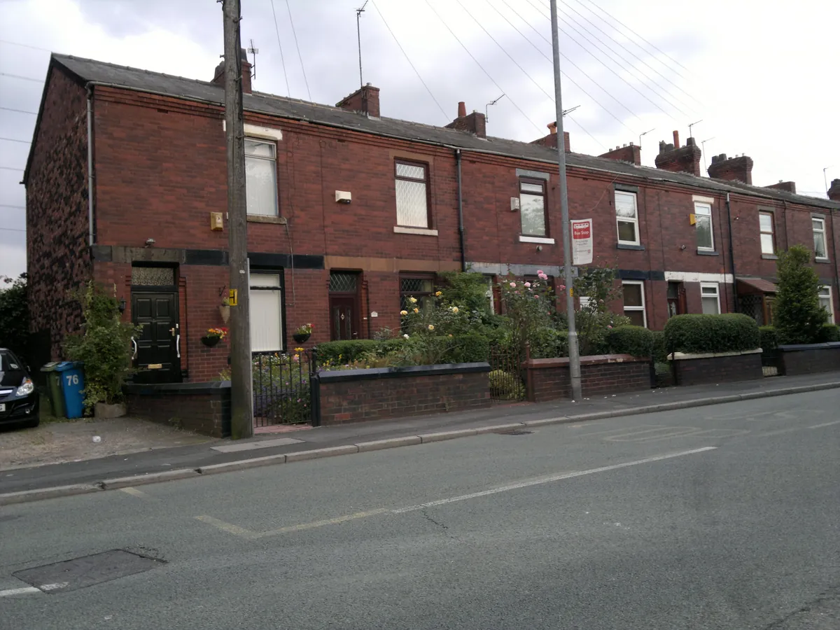 A row of brick terraced houses with small front gardens on Mills Hill Road, Chadderton