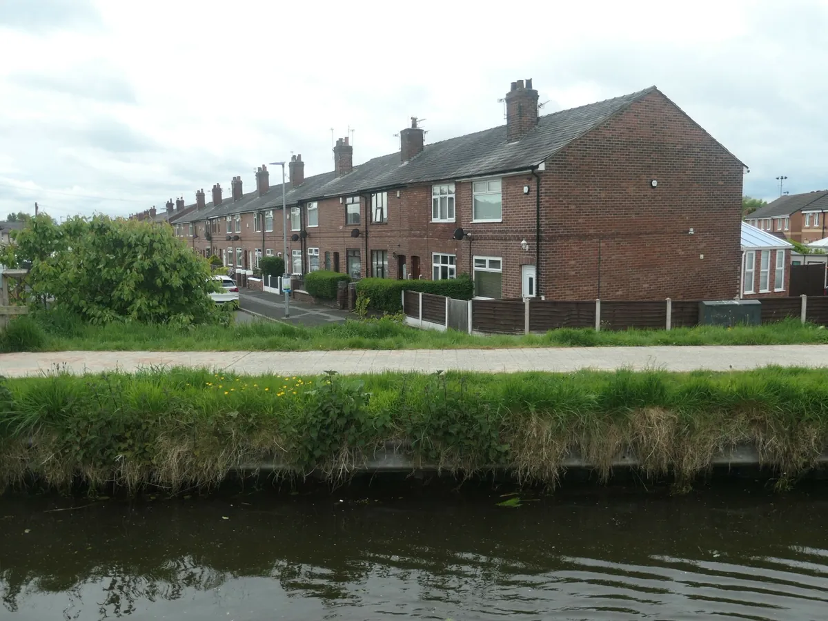 A row of red-brick terraced houses on Lilford Street in Leigh, seen across the canal